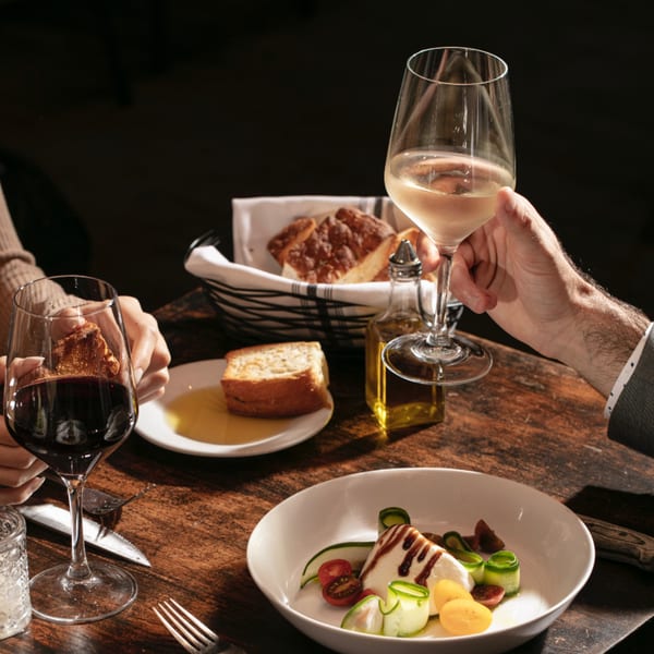 Diners at (aged.) bistro enjoying wine, bread, olive oil, and a caprese salad.