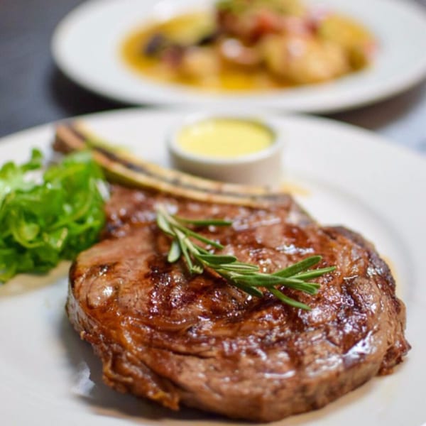 Aged bistro steak with rosemary, greens, and a side of sauce on a white plate.