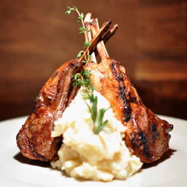 Grilled lamb chops with mashed potatoes and fresh herbs on a white plate at (aged.) bistro.