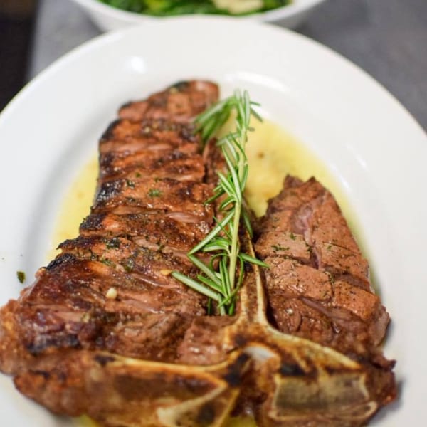 Grilled T-bone steak with rosemary sprig and mashed potatoes on a white plate.