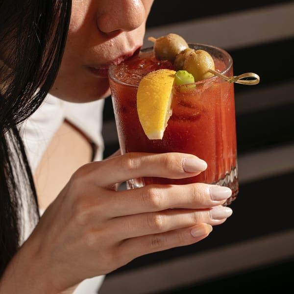 A person sips a Bloody Mary garnished with olives and a lemon slice.