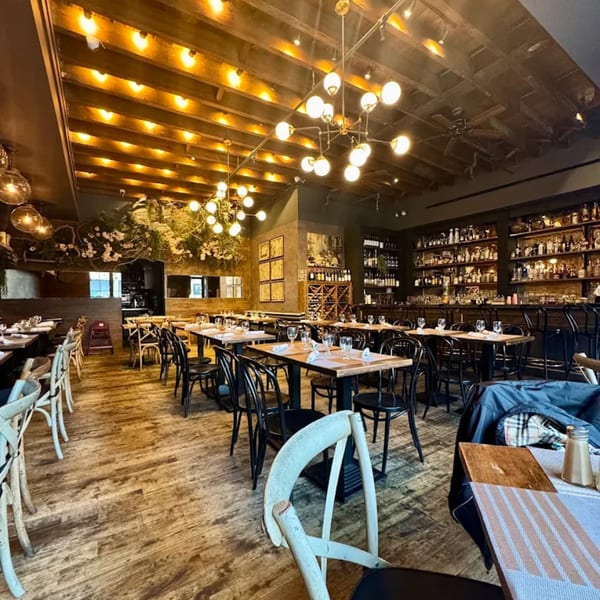 Aged bistro interior with wooden floors, exposed beam ceiling, modern chandeliers, and a full bar.
