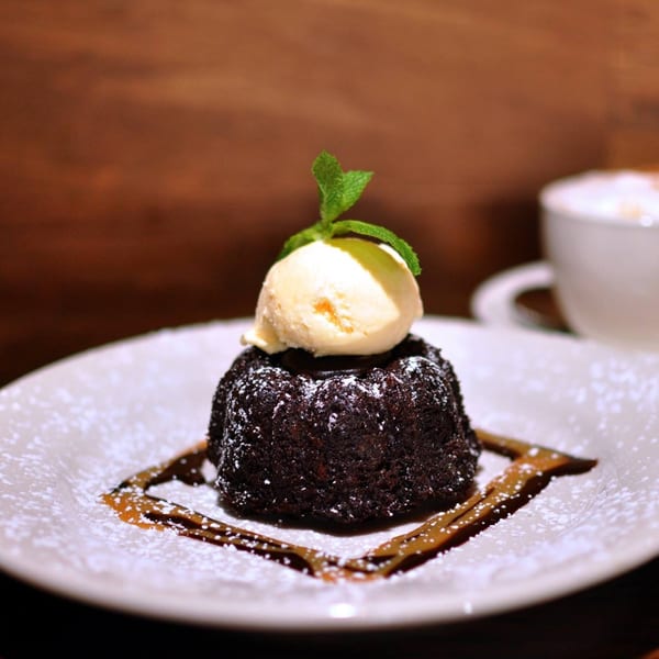 A rich chocolate lava cake with a scoop of vanilla ice cream and mint on a white plate.