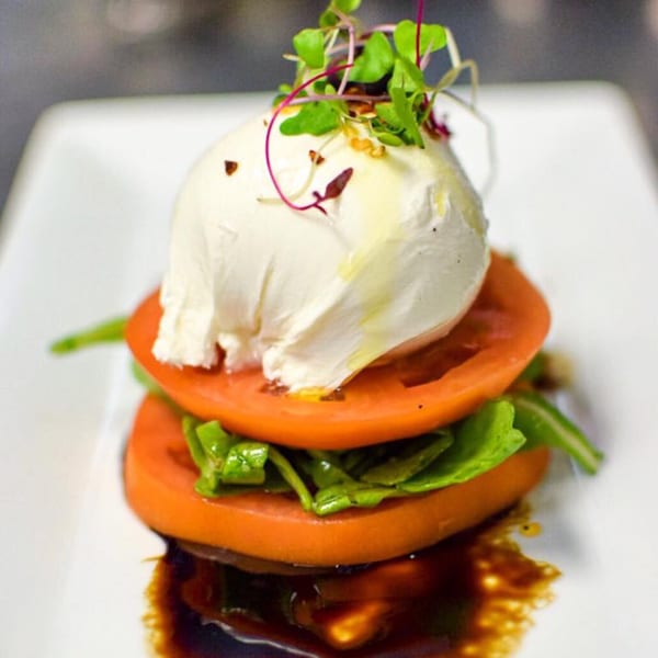 Caprese salad with fresh mozzarella, sliced tomatoes, arugula, and balsamic glaze on a white plate.